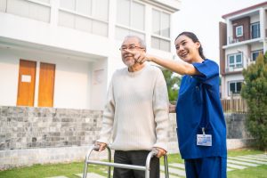 Asian young caregiver nurse support senior older male walking outdoors.