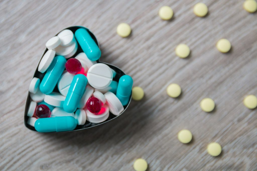 Heart from colorful medication and pills above on grey wooden background.