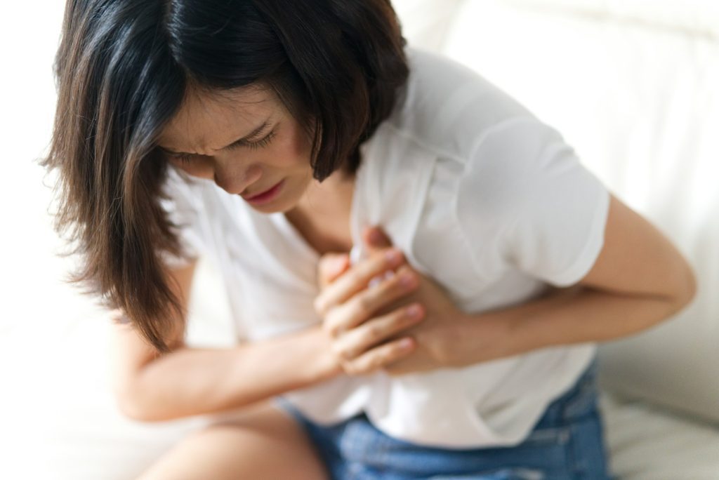 Unwell condition and sickness concept; Asian woman having heart attack sitting on sofa.